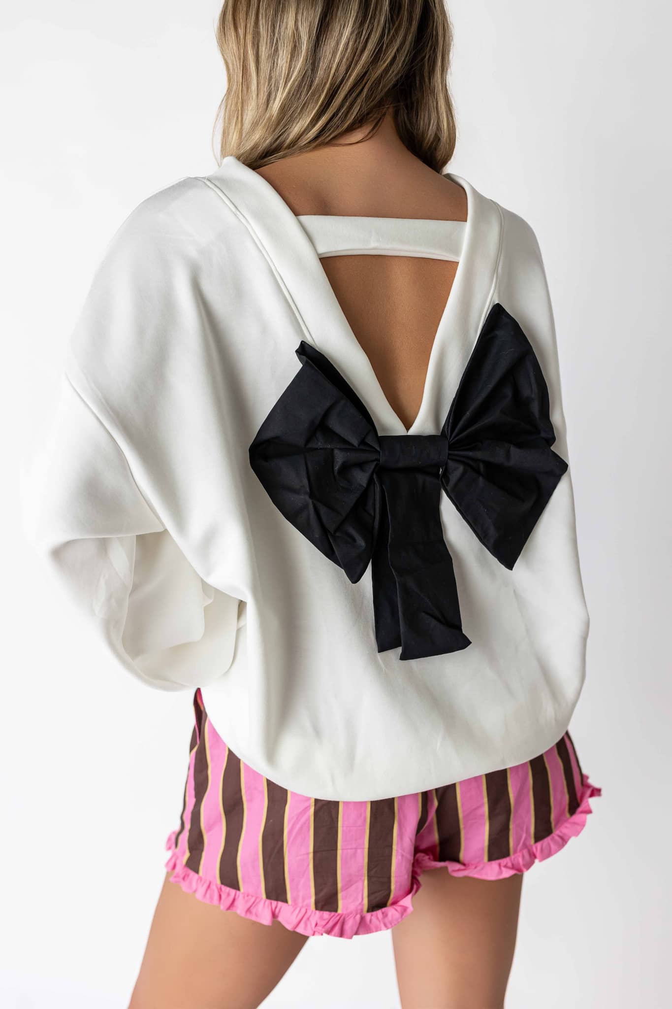 White back bow sweatshirt with large black bow detail worn with striped pink shorts