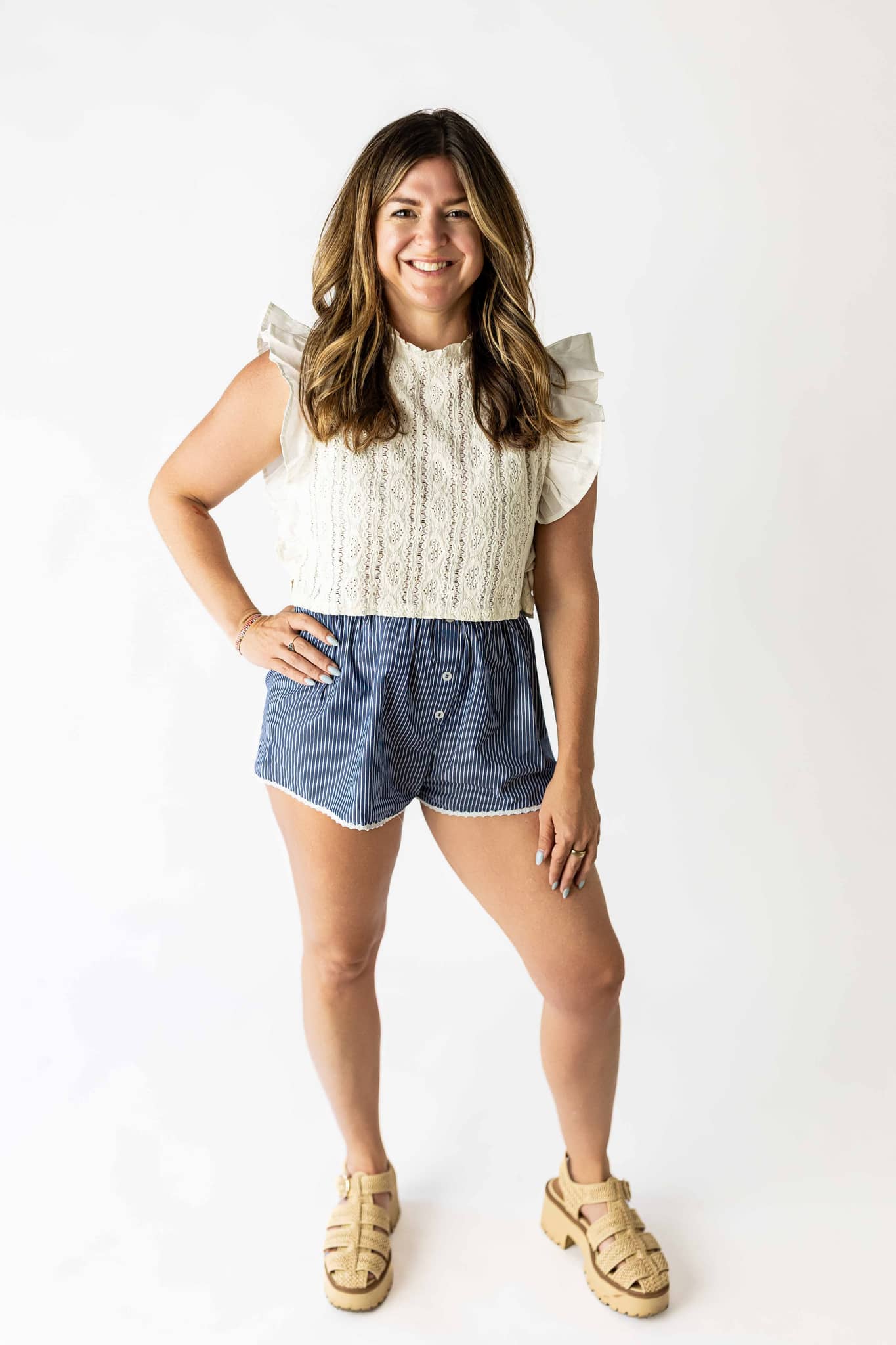 Woman wearing a white ruffle sleeve lace top paired with blue shorts and beige sandals