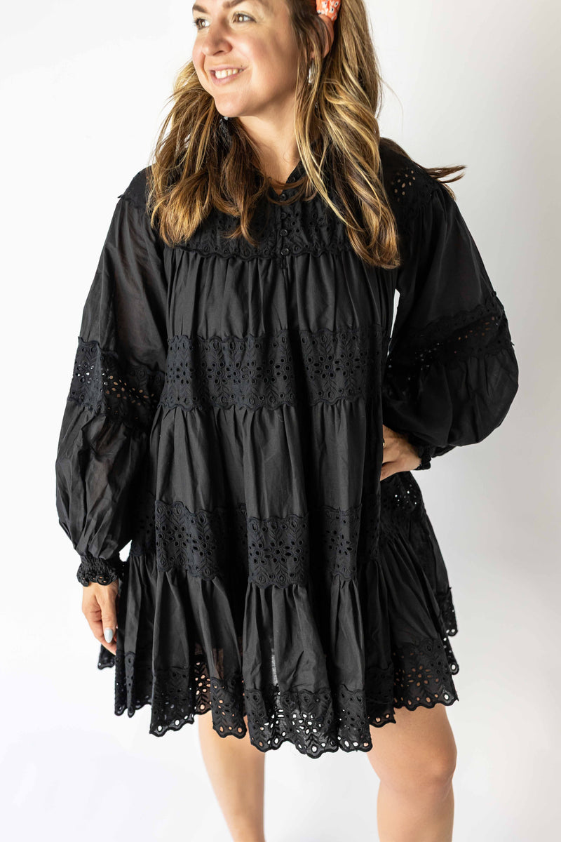 Woman wearing black long sleeve eyelet mini dress with intricate lace details and a loose fit