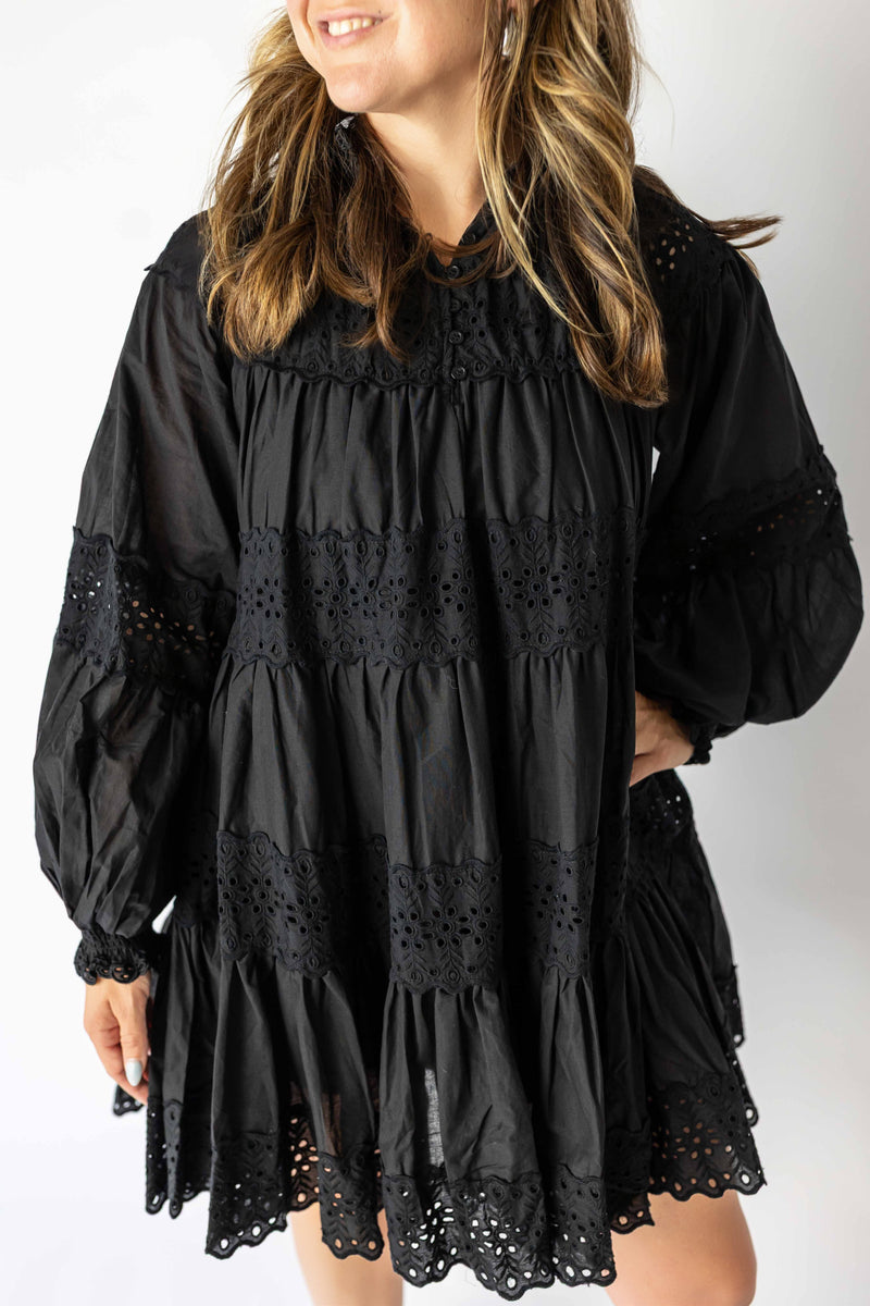 Black long sleeve eyelet mini dress with intricate lace detailing and tiered design