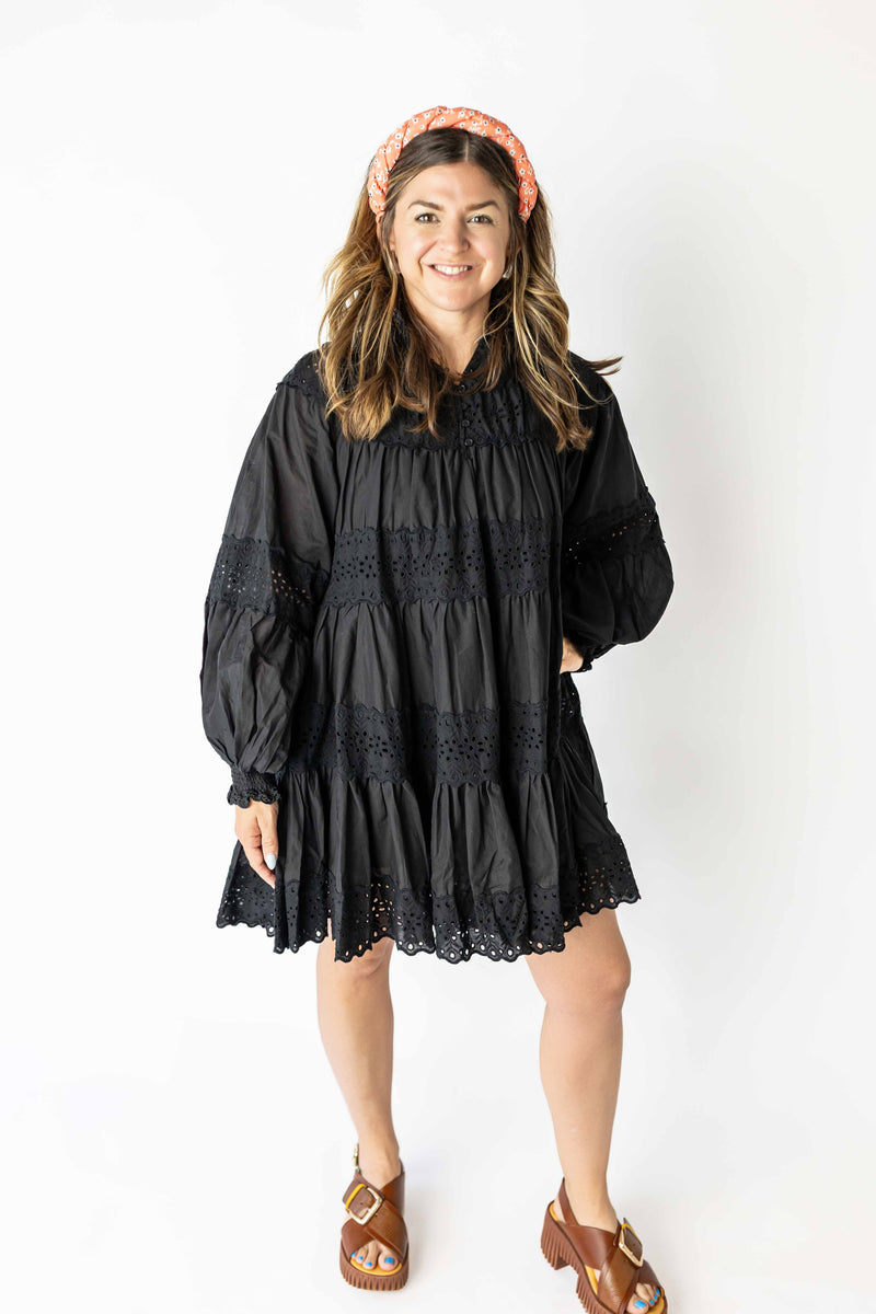 Smiling woman wearing black long sleeve eyelet mini dress with ruffled hem and puff sleeves