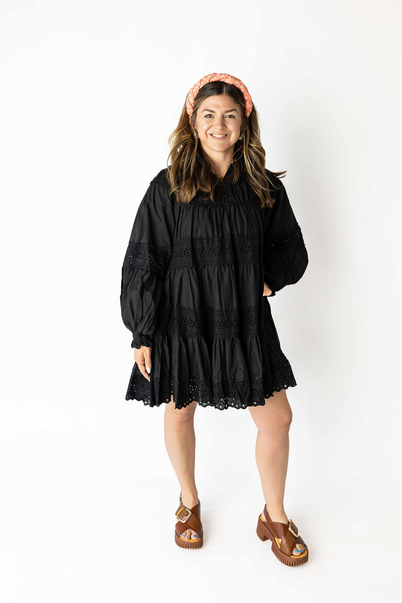 Woman wearing a black long sleeve eyelet mini dress with scalloped hem and puff sleeves