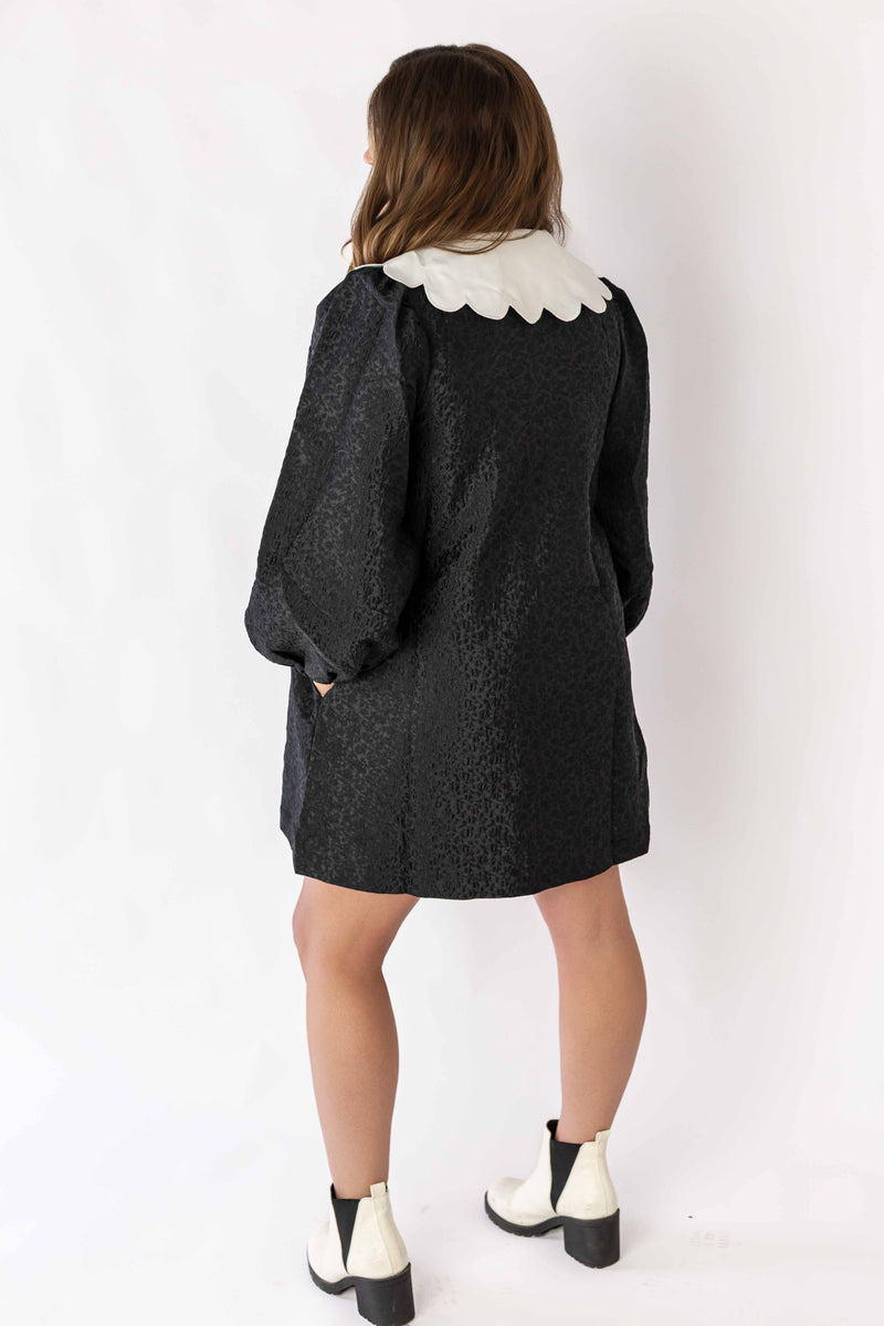 Back view of a black mini dress with collar and puffed sleeves paired with white ankle boots