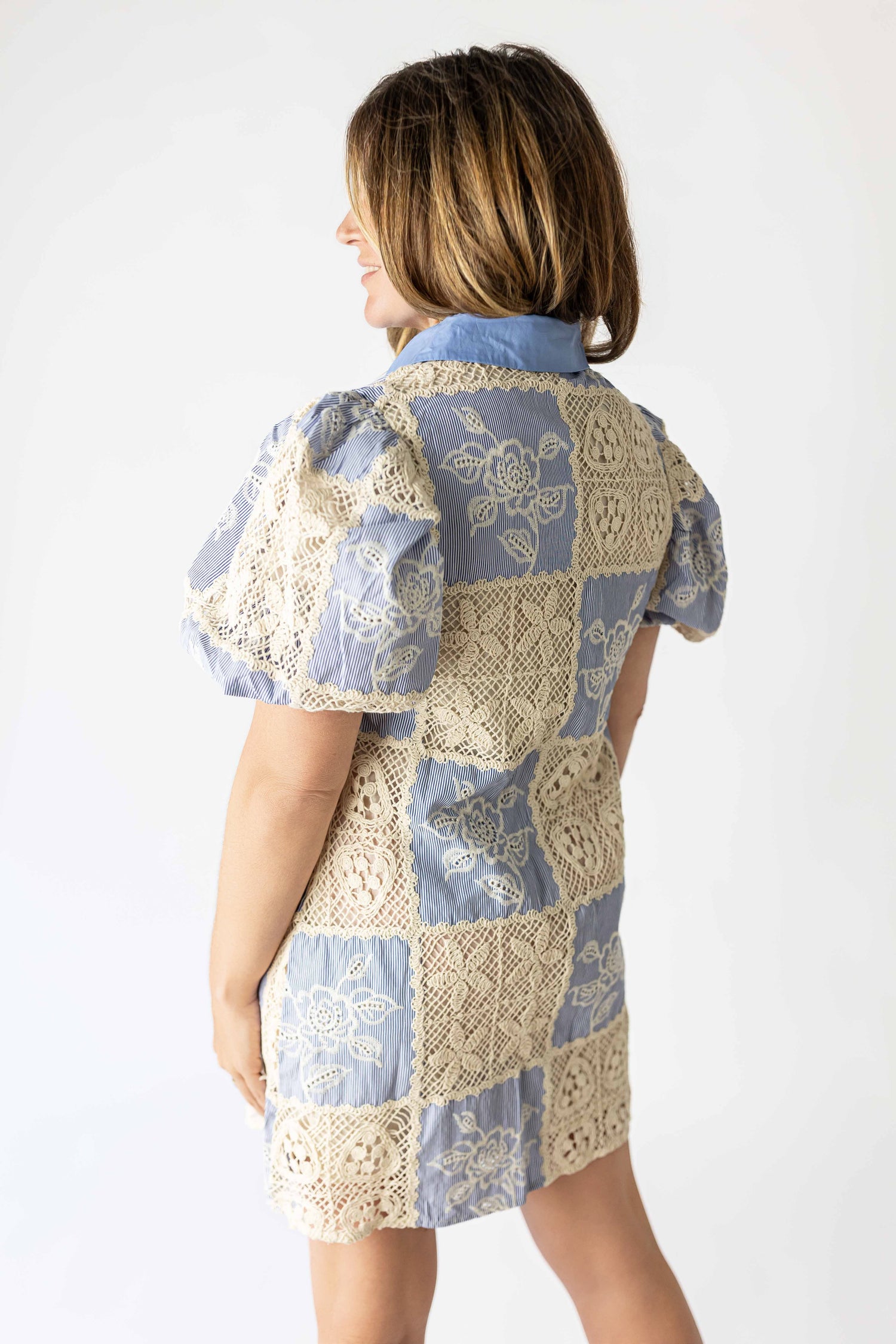 Back view of a woman wearing a boho patchwork crochet dress with blue and beige floral crochet patches