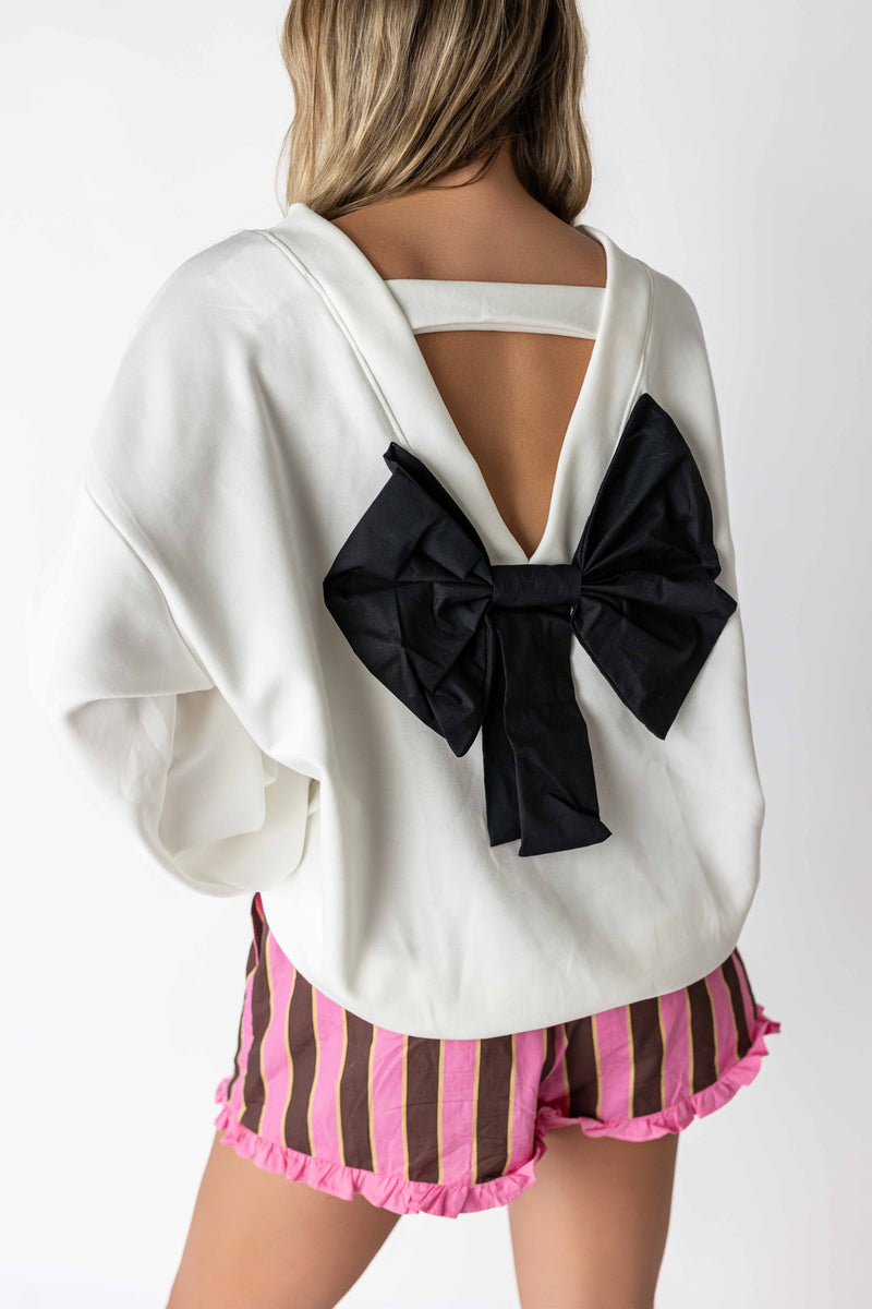 White back bow sweatshirt with large black bow detail worn with striped pink shorts