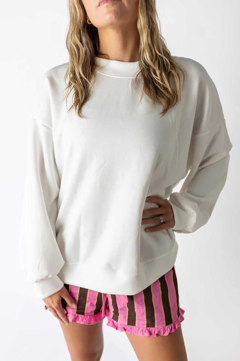 White back bow sweatshirt with long sleeves worn by a woman with striped pink and brown shorts