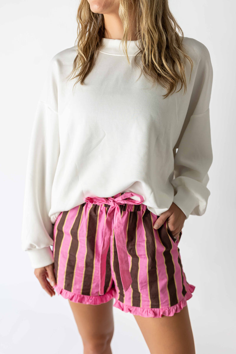 White back bow sweatshirt paired with pink and brown striped shorts with ruffle hem