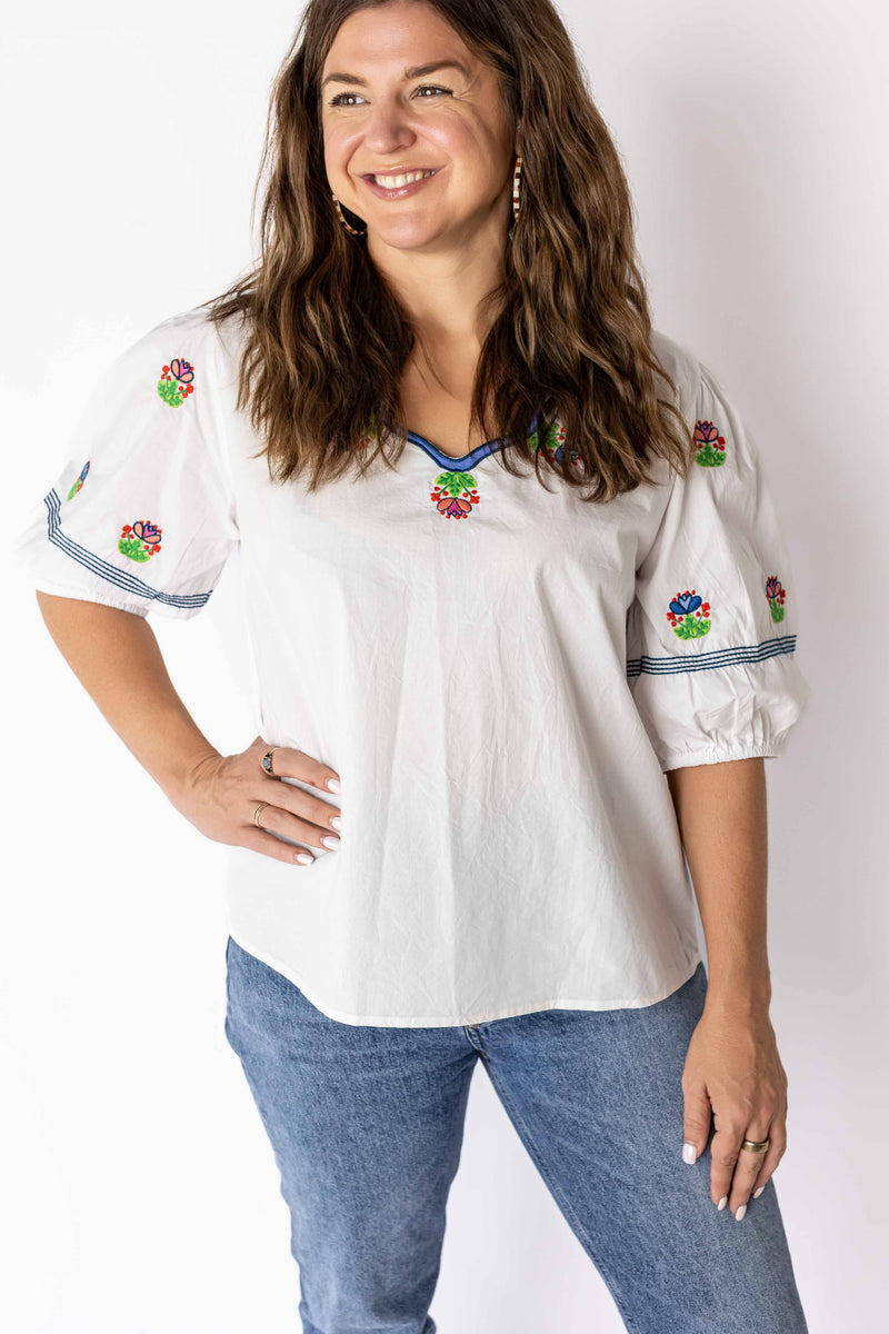 Weaving Color white embroidered peasant top with colorful floral designs and puff sleeves worn by woman