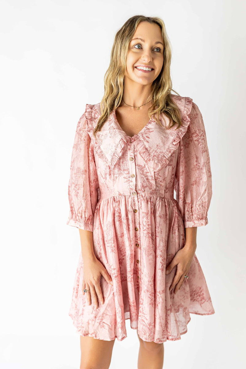 Smiling woman wearing a pink feminine floral print dress with ruffled collar and buttons