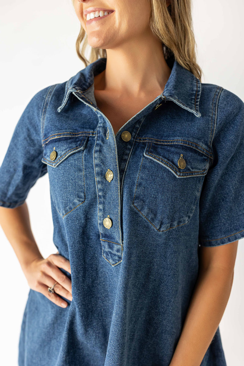 Close-up of a woman wearing a medium wash denim dress with short sleeves and button-down front