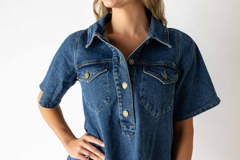 Close-up of a woman wearing a medium wash denim dress with short sleeves and front button details