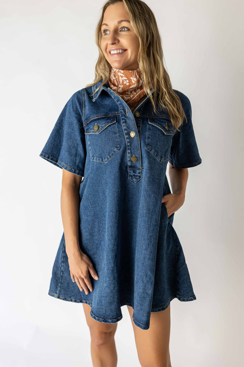 Woman wearing a short sleeve medium wash denim dress with front button details and pockets