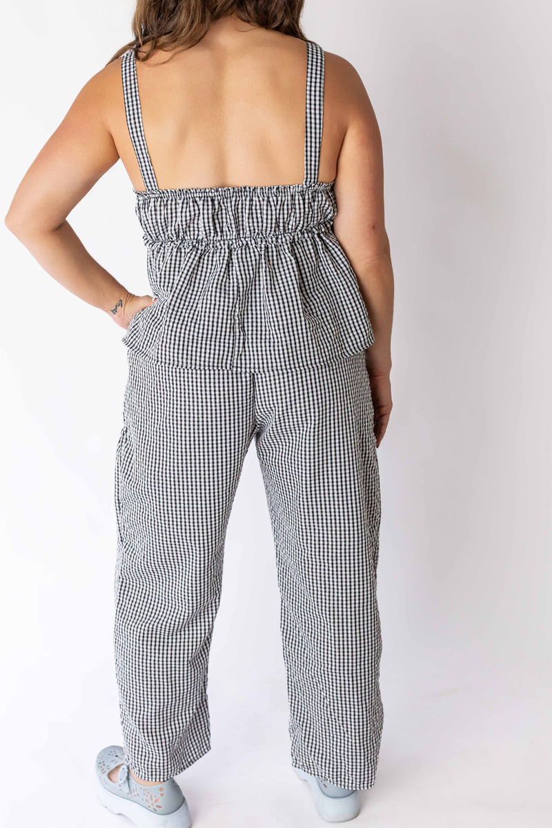 Back view of woman wearing black and white gingham relaxed pants with matching top and light blue shoes