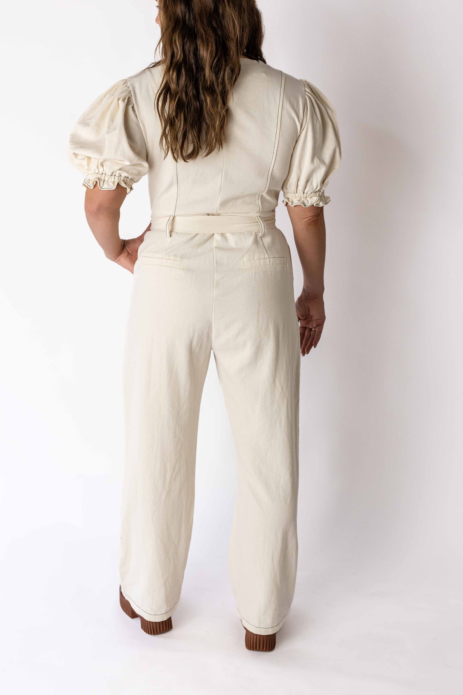 Back view of woman wearing ivory puff sleeve jumpsuit by Weaving Color with high waist and cuffed sleeves