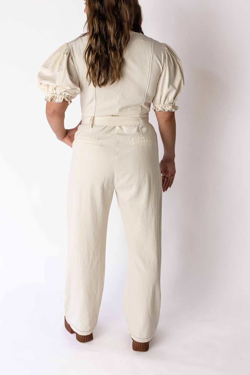 Back view of woman wearing ivory puff sleeve jumpsuit by Weaving Color with high waist and cuffed sleeves