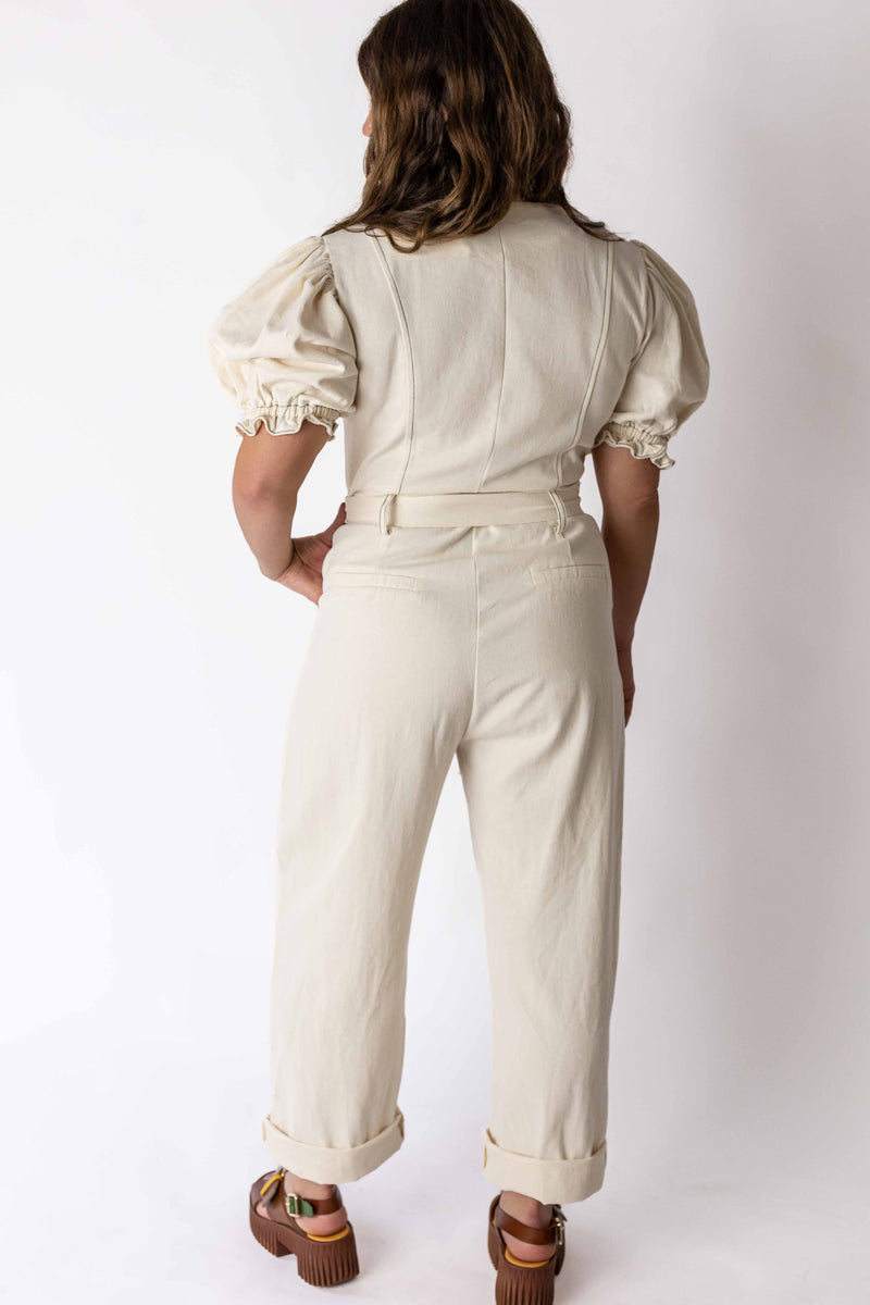 Back view of woman wearing ivory puff sleeve jumpsuit by Weaving Color with rolled cuffs and brown sandals