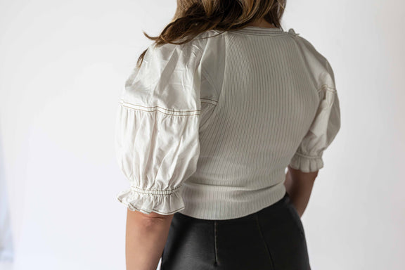 Back view of woman wearing white kora puff sleeve top with textured fabric and elastic cuffs