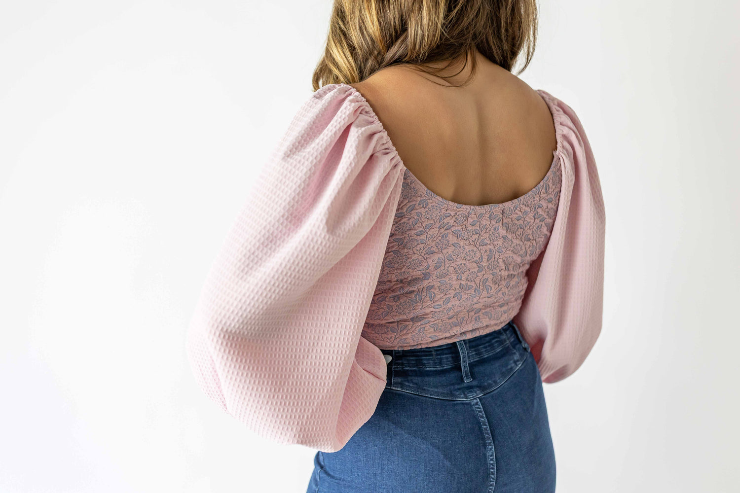 Back view of lavender puff sleeve bodysuit with textured fabric and patterned torso paired with blue jeans