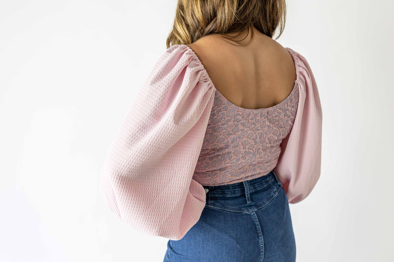 Back view of lavender puff sleeve bodysuit with textured fabric and patterned torso paired with blue jeans