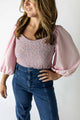Woman wearing lavender puff sleeve bodysuit with lace detail and high-waisted blue jeans