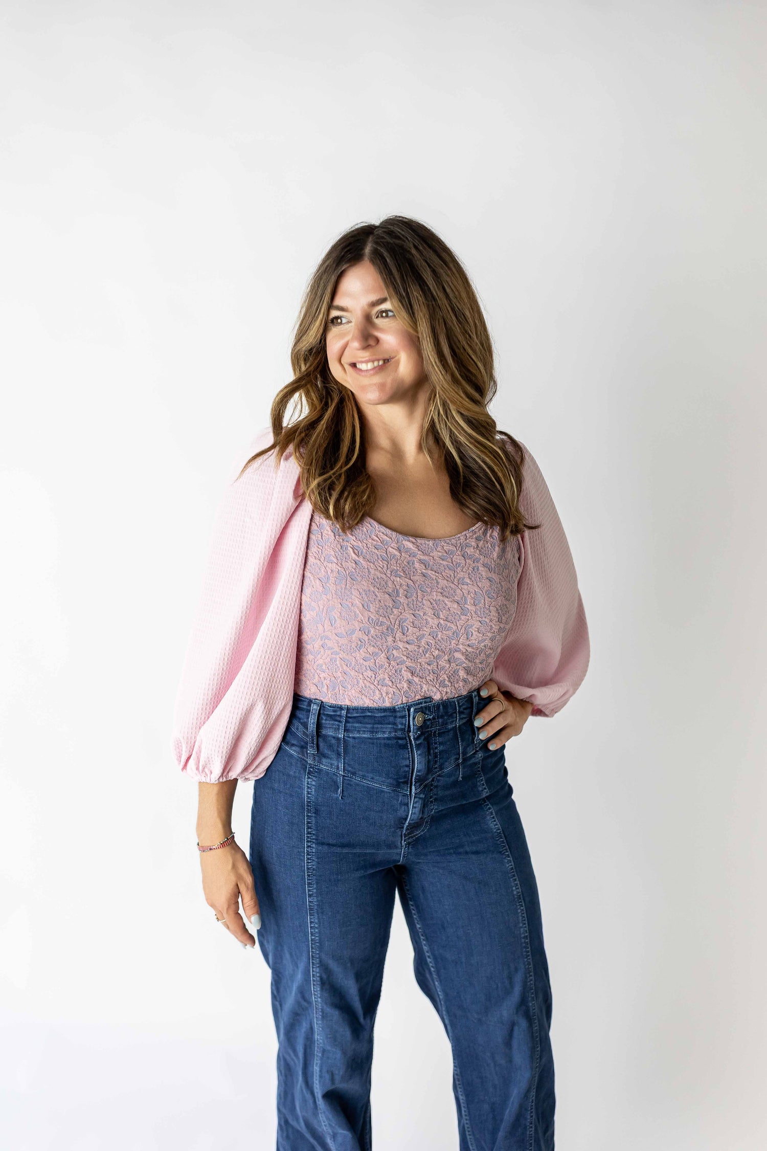 Woman wearing lavender puff sleeve bodysuit paired with high-waisted blue jeans smiling