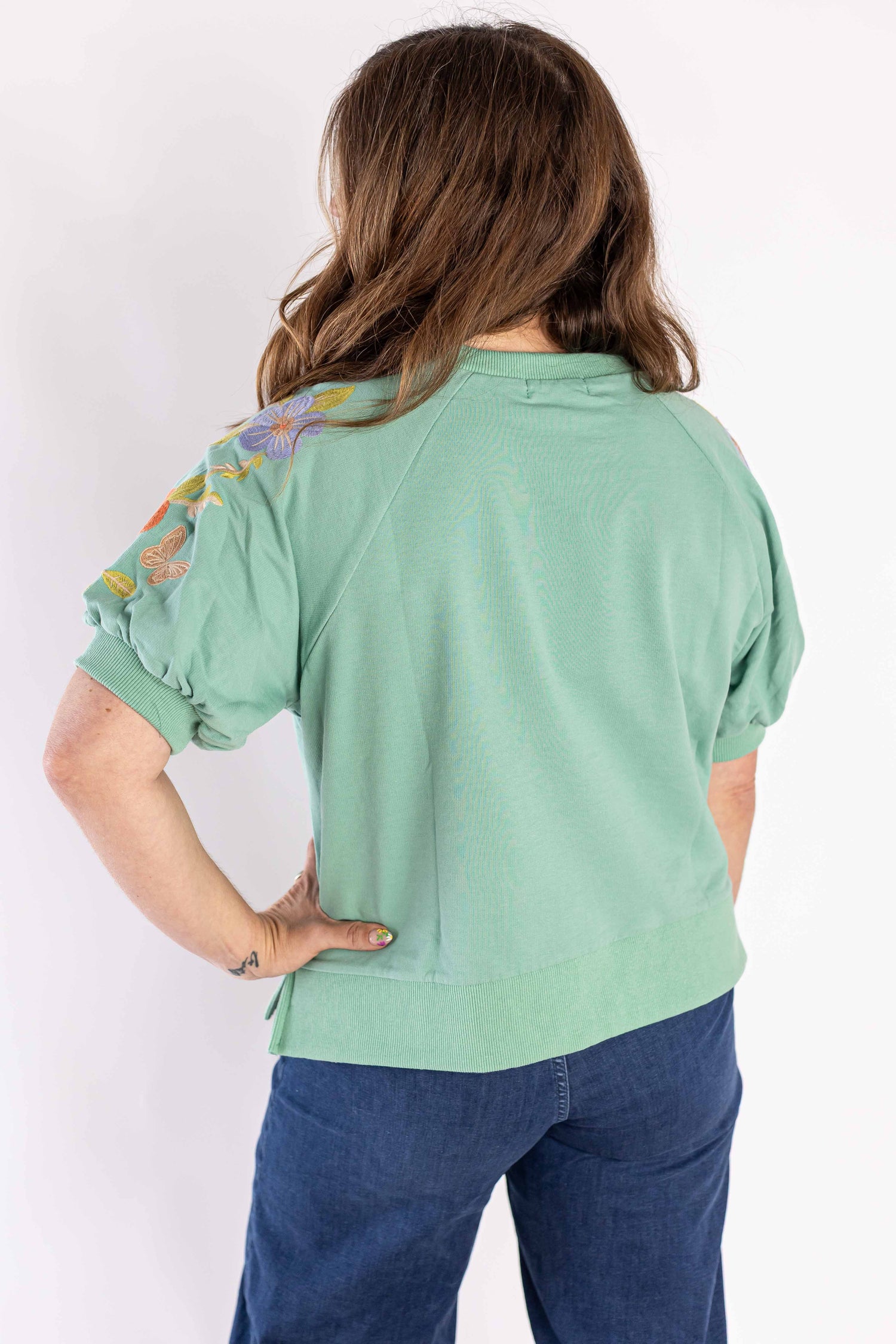 Back view of a woman wearing a green mineral bloom sweatshirt with floral embroidery on the sleeves