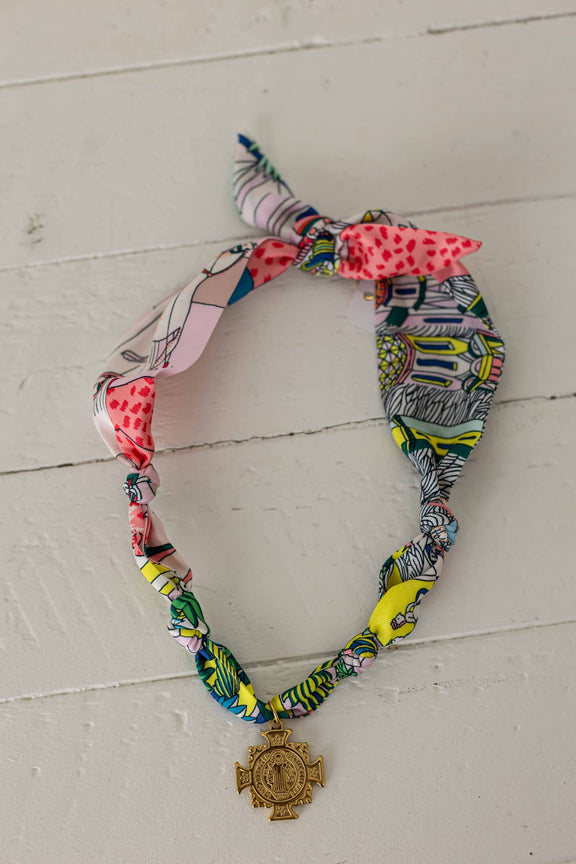 Weaving Color colorful scarf necklace with mixed patterns and gold cross pendant on white wooden surface