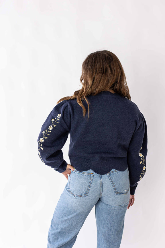 Back view of woman wearing navy blue daisy chain sweater with floral embroidery on sleeves by Weaving Color