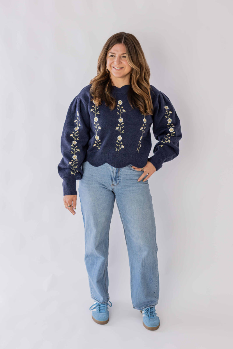 Woman wearing Weaving Color navy blue daisy chain sweater with floral embroidery and light blue jeans