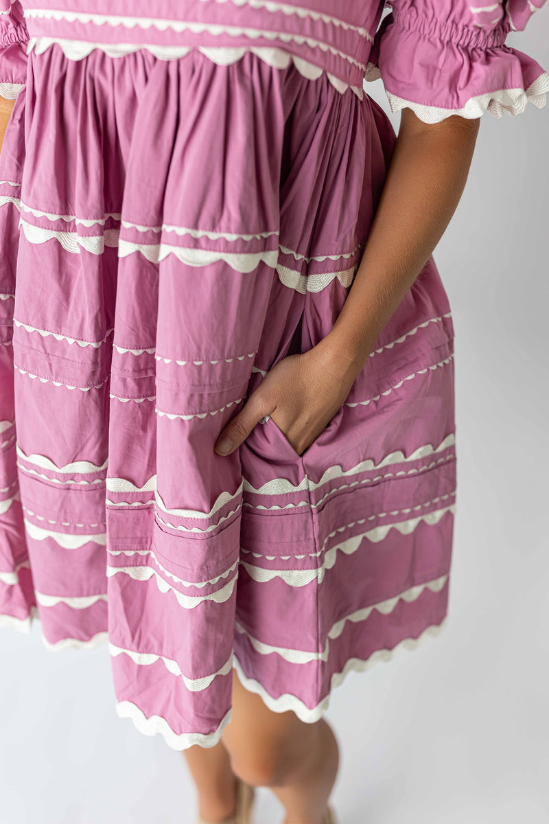 Close-up of pink puff sleeve mini dress with white scalloped trim and a hand in the pocket