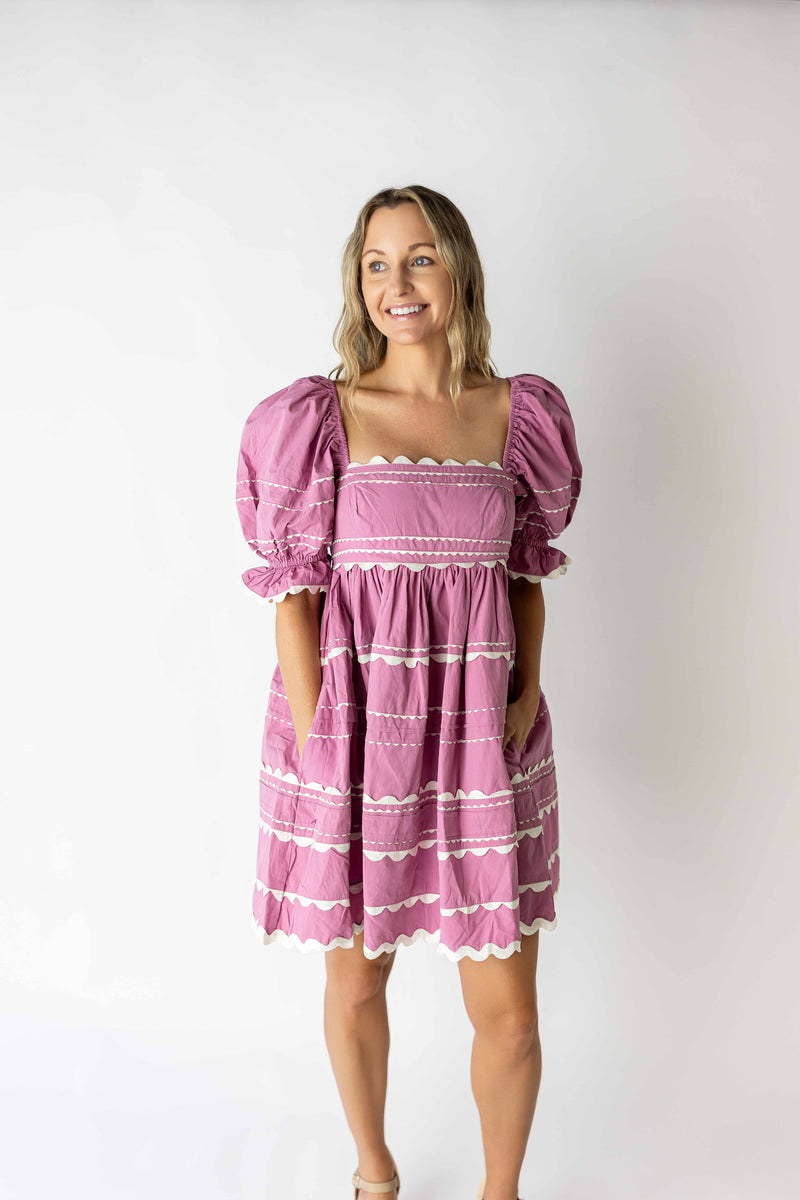 Woman wearing a pink puff sleeve mini dress with lace trim and pockets in a studio setting