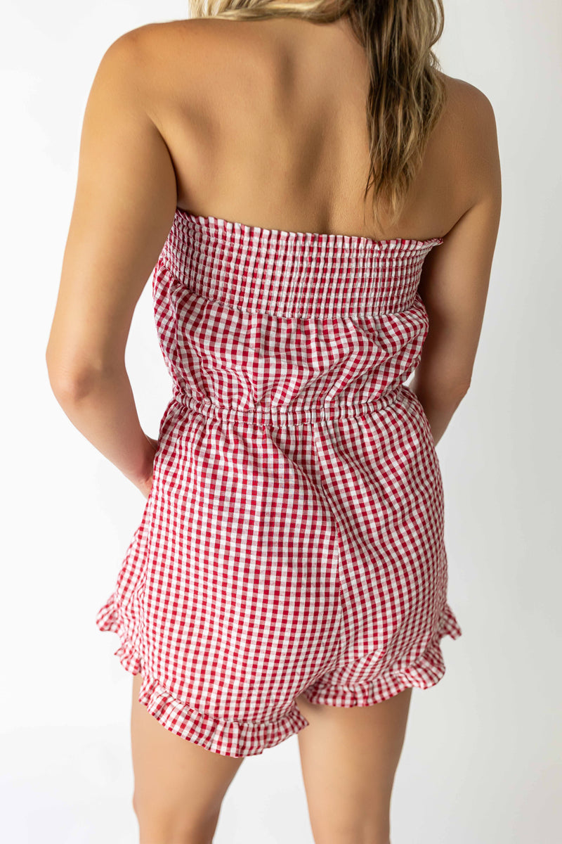 Back view of a woman wearing a red checkered tube romper with ruffled shorts and smocked bodice