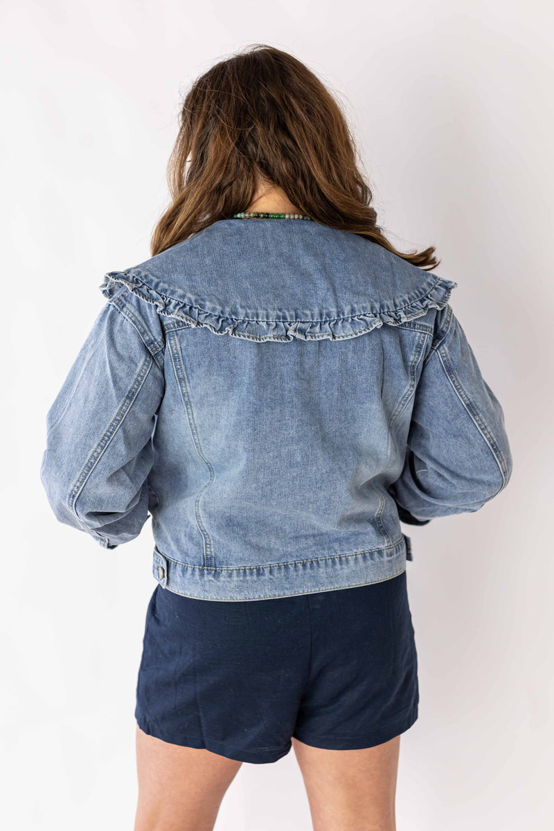 Back view of woman wearing ruffle collar denim jacket by Weaving Color with puff sleeves and light wash