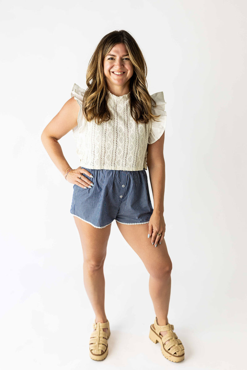 Woman wearing a white ruffle sleeve lace top paired with blue shorts and beige sandals