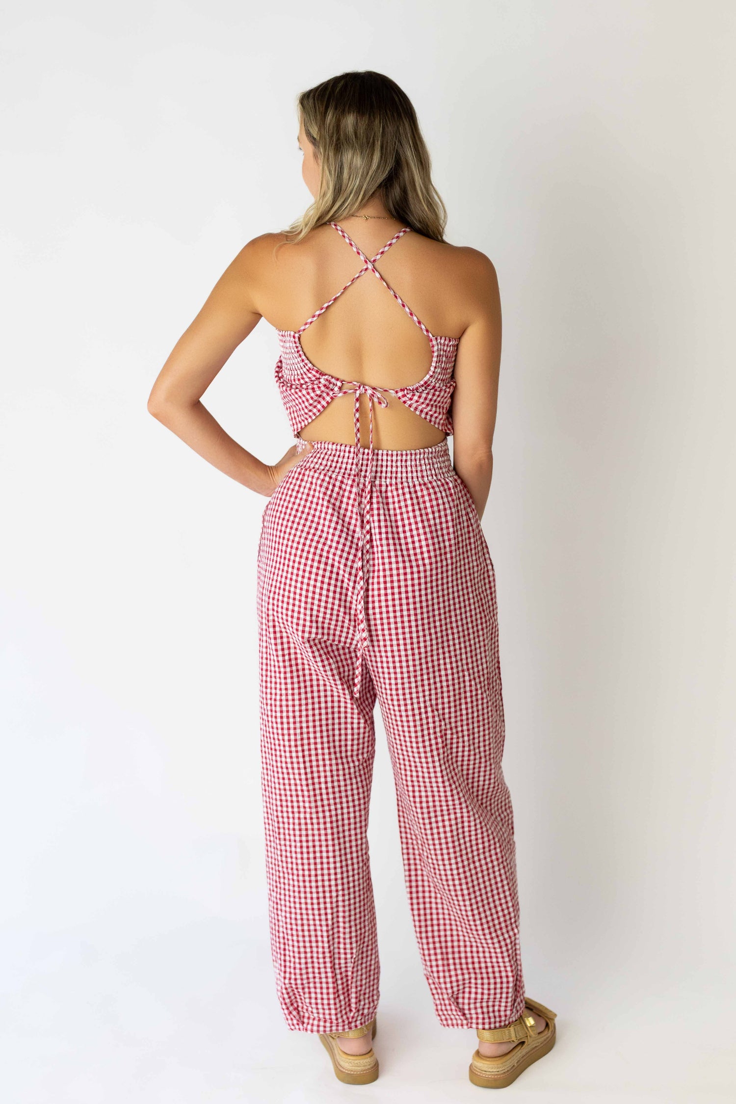 Back view of woman wearing red and white seersucker check jumpsuit with crisscross straps