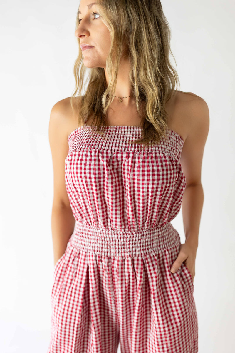 Woman wearing red and white strapless seersucker check jumpsuit with smocked waist and pockets