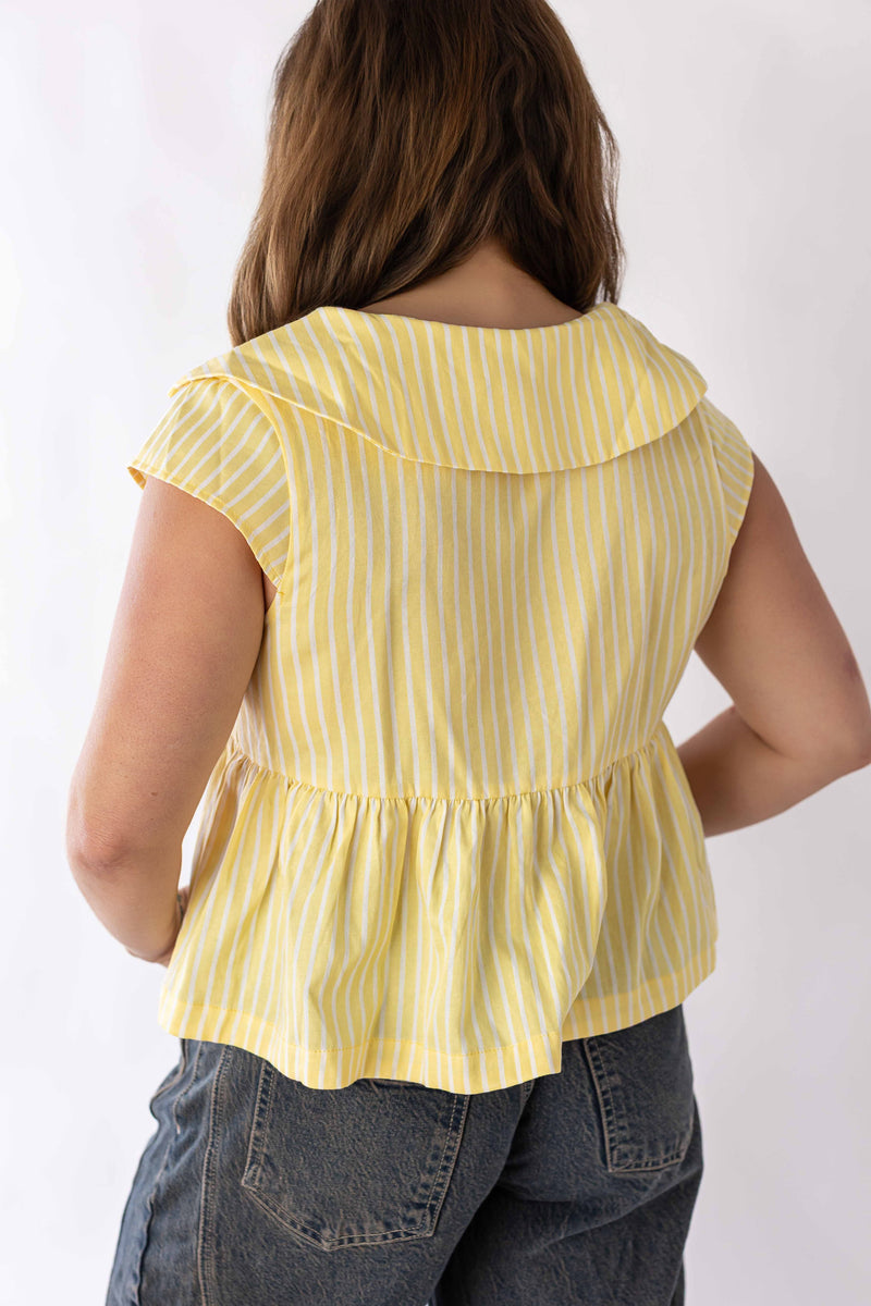 Back view of woman wearing yellow and white sunshine stripe peplum blouse with cap sleeves and ruffled hem