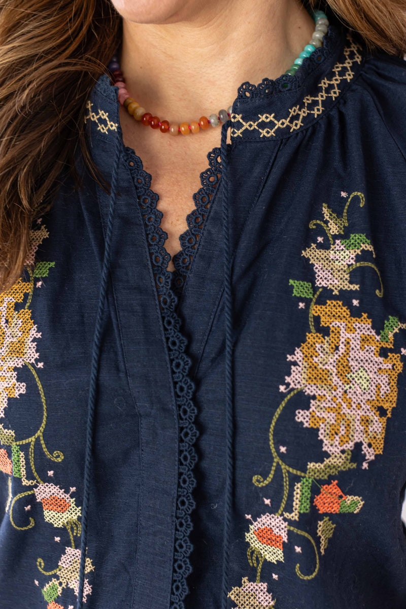 Close-up of embroidered bloom romper by Weaving Color in navy with detailed floral embroidery and lace trim