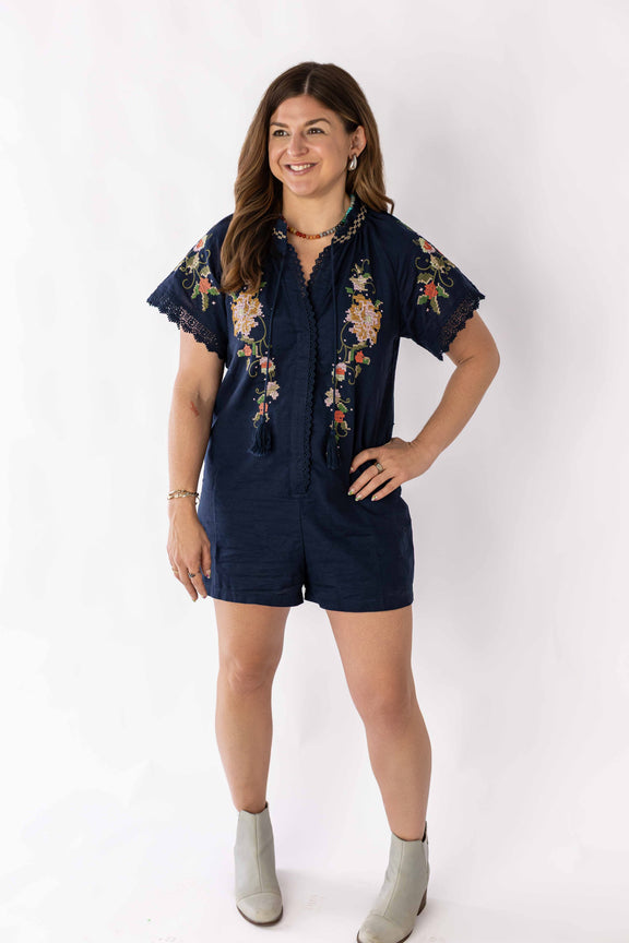 Woman wearing navy blue embroidered bloom romper with floral designs and short sleeves
