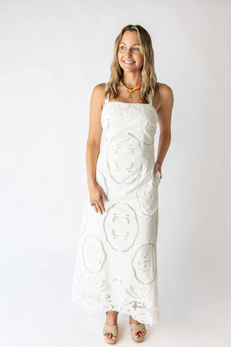 Smiling woman wearing a white crochet maxi dress with floral patterns and pockets