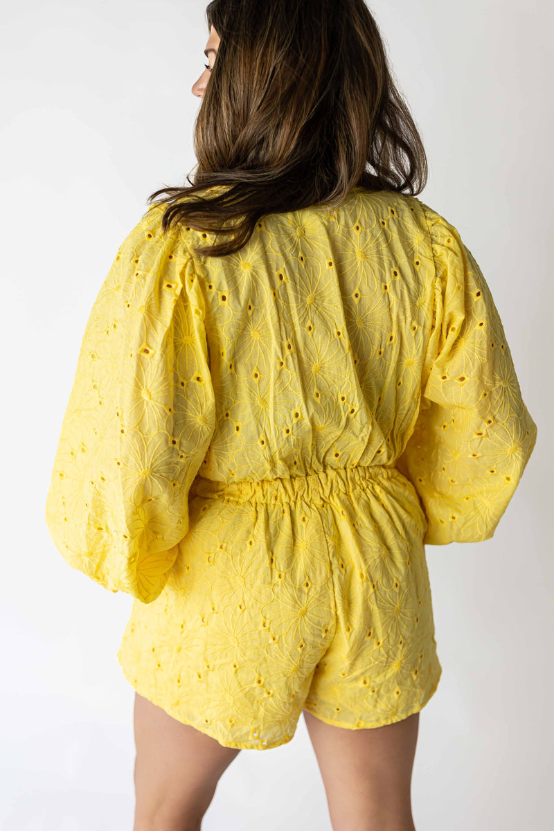 Back view of a woman wearing a yellow eyelet romper with long sleeves and elastic waistband